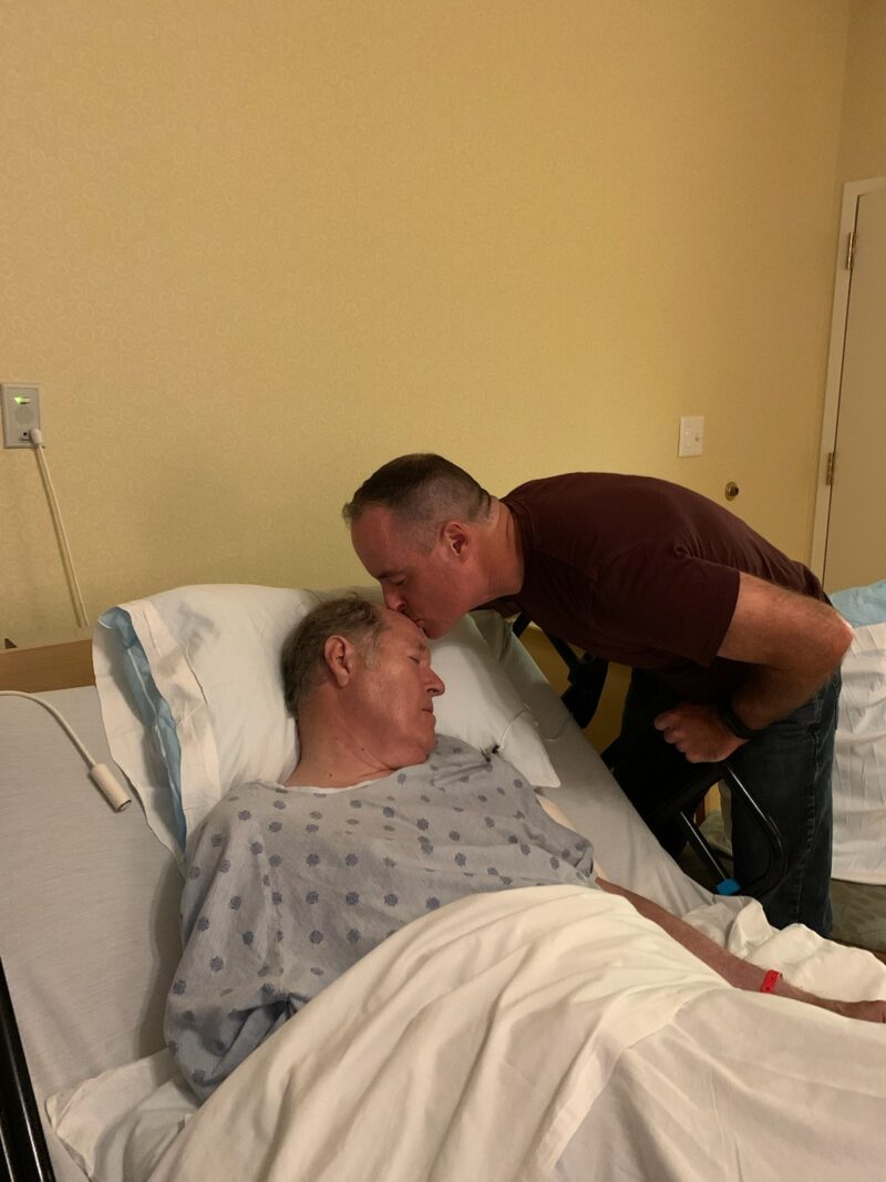 Man kissing his elderly father in hospital bed in hospital