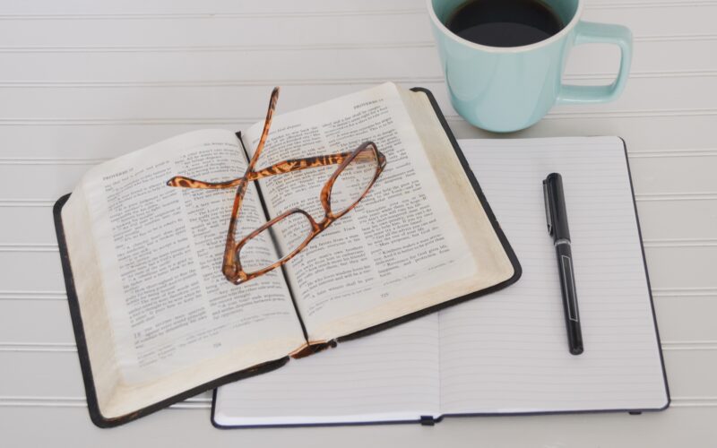 Bible and journal on table with mug of black coffee