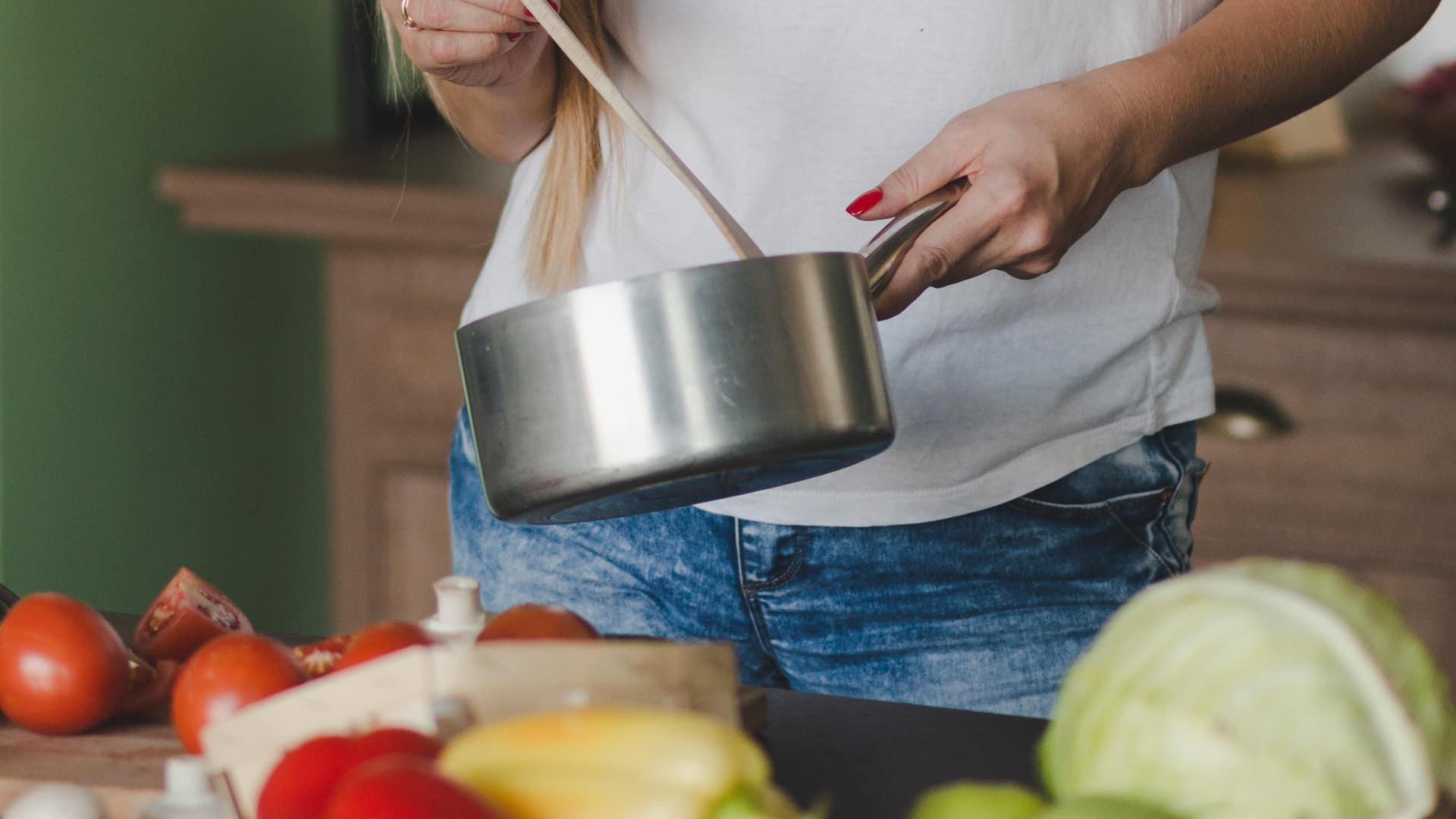 Woman cooking with metal pan in kitchen.