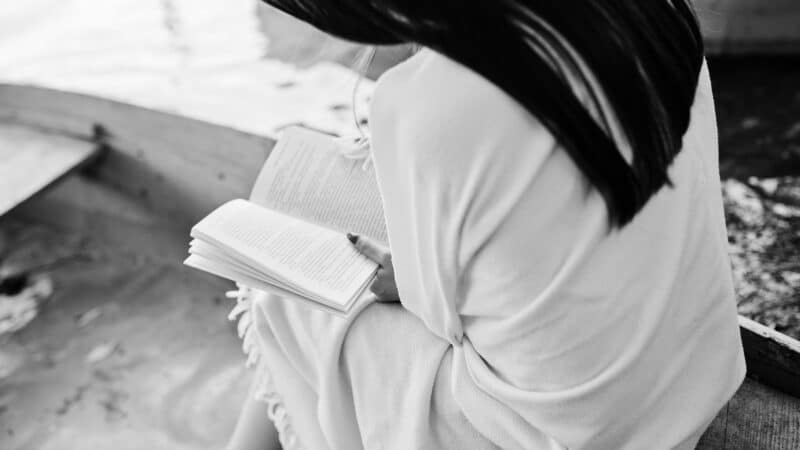 Woman reading Bible by the water.