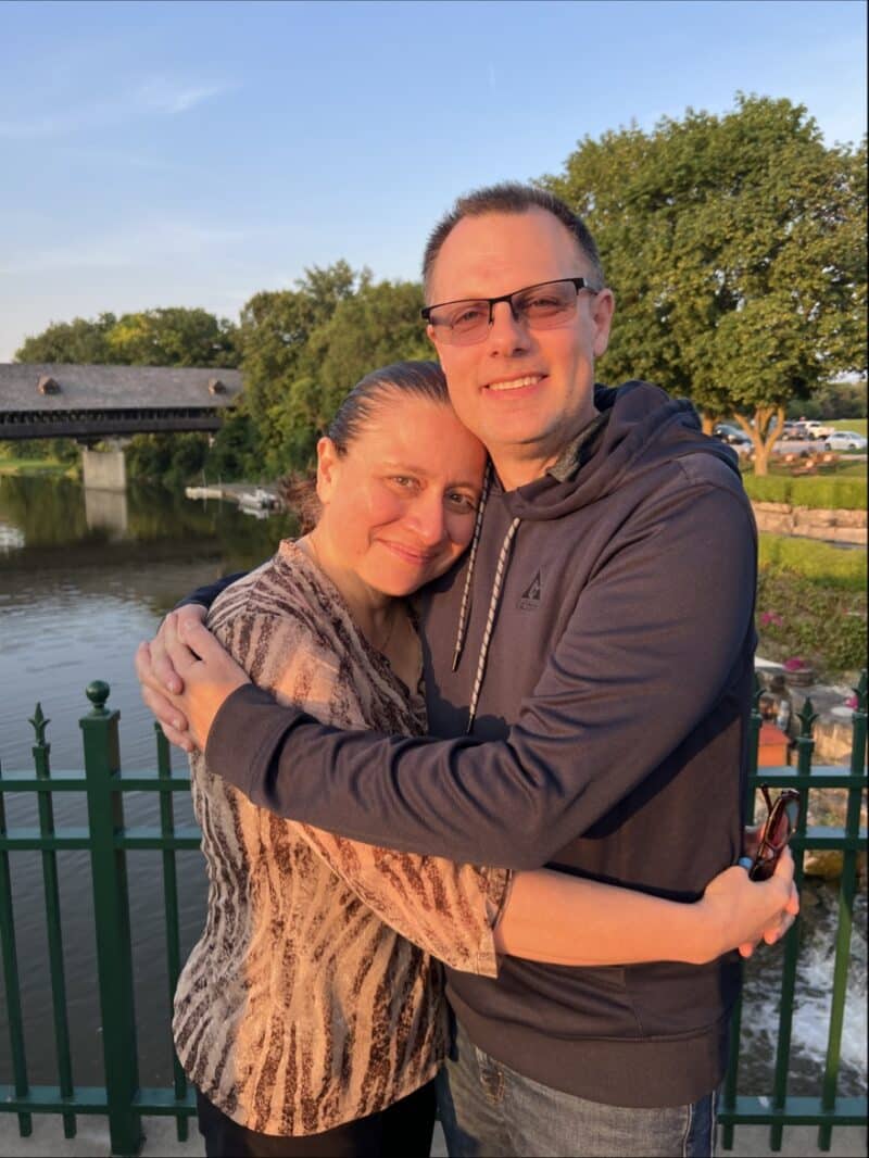 Man and Wife Hugging and standing in from of a lake.