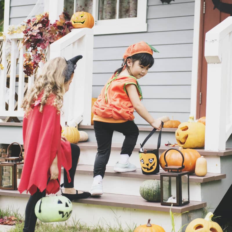Girls walking up the steps to trick or treat in pumpkin and cat costumes.