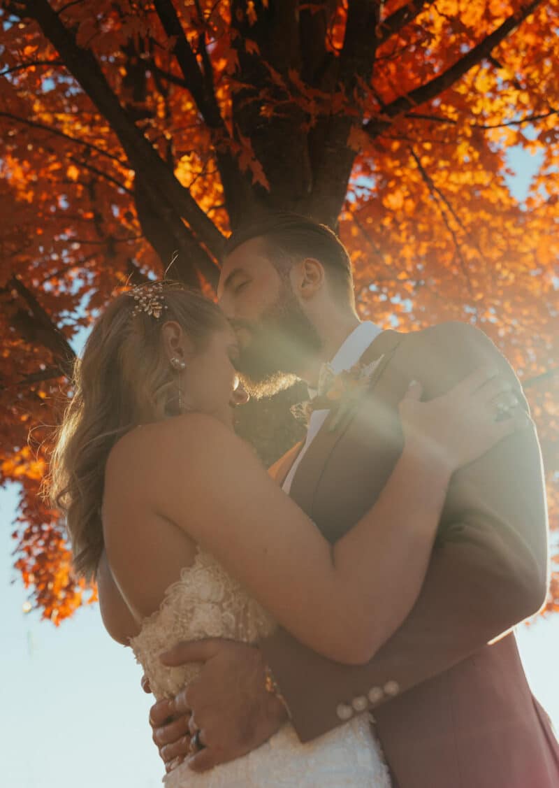 Sweet wedding kiss in front of autumn tree